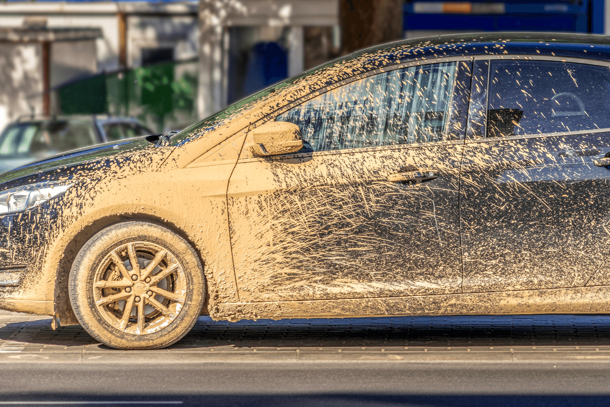 A black sedan heavily covered in dried mud and road grime.